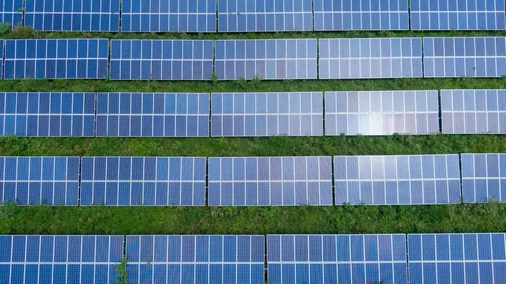 Aerial view of rows of blue solar panels installed on a grassy field, arranged in parallel lines and evenly spaced