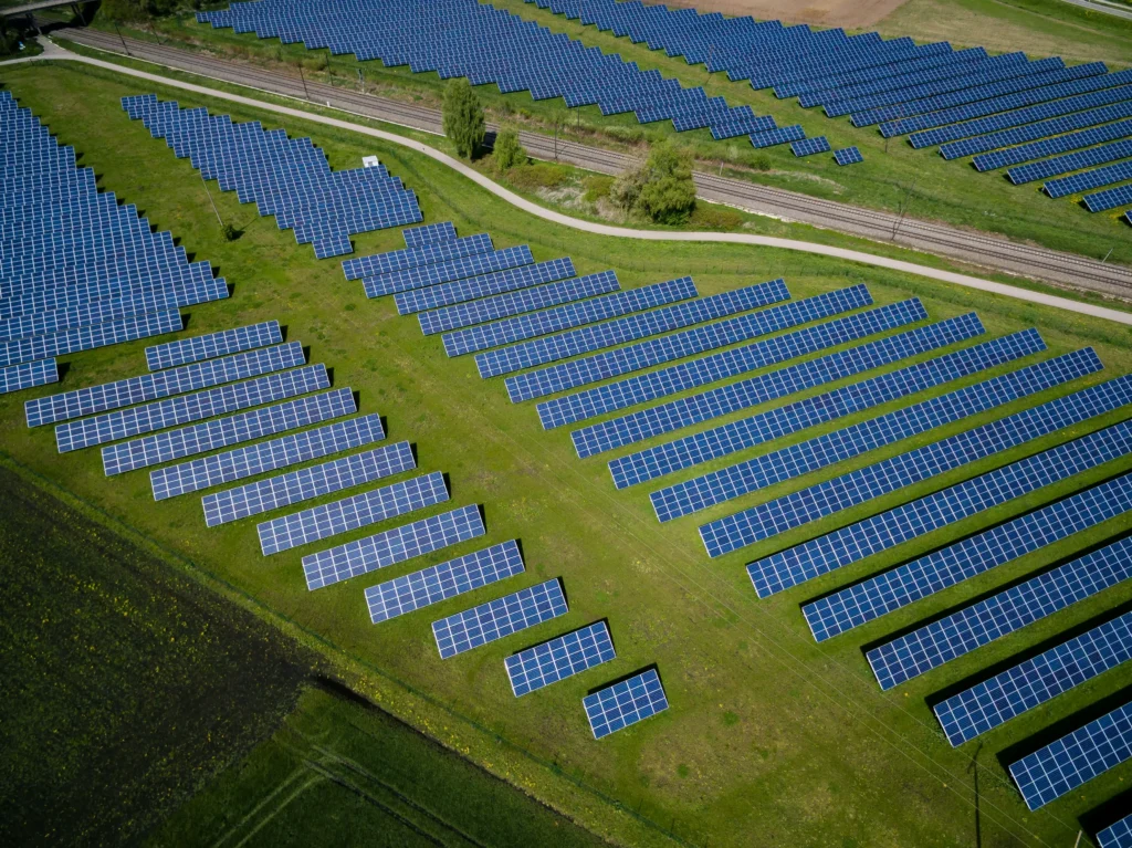 Aerial view of a solar farm with rows of blue panels on green fields